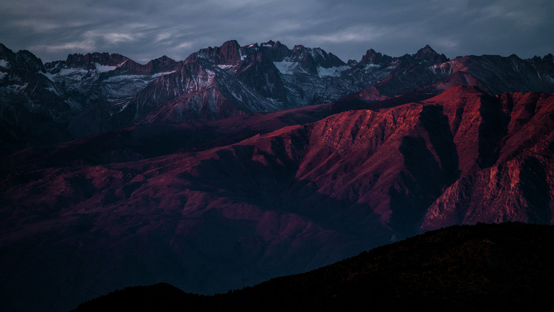 Rugged dark mountain ridges glowing under a dusky cloudy sky