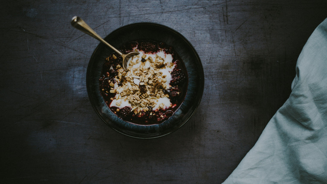 Black bowl of oats and berries with a spoon on dark slate