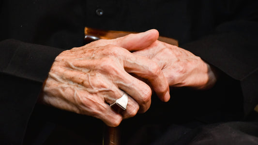 Older person's hands resting on a walking cane, dark background