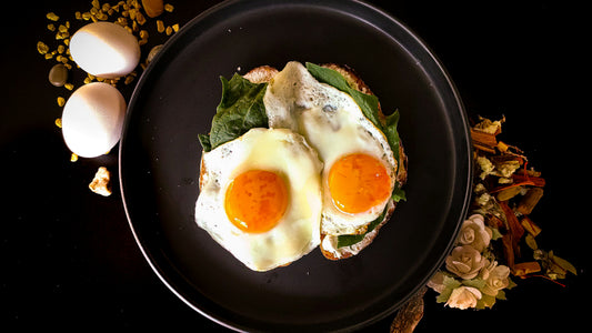 Fried eggs on greens on a black plate with whole eggs beside