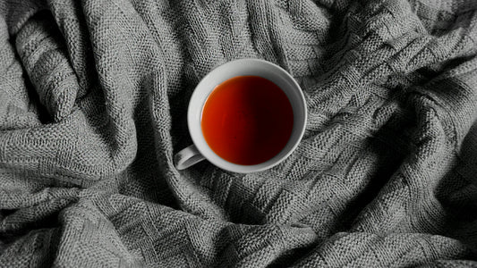 Cup of dark red herbal tea on a grey knitted blanket
