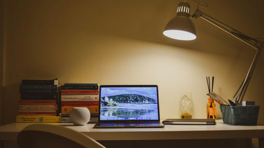 Open laptop and books on a desk lit by a warm lamp