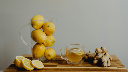 Lemons, sliced lemon, glass of ginger tea and fresh ginger on wooden table