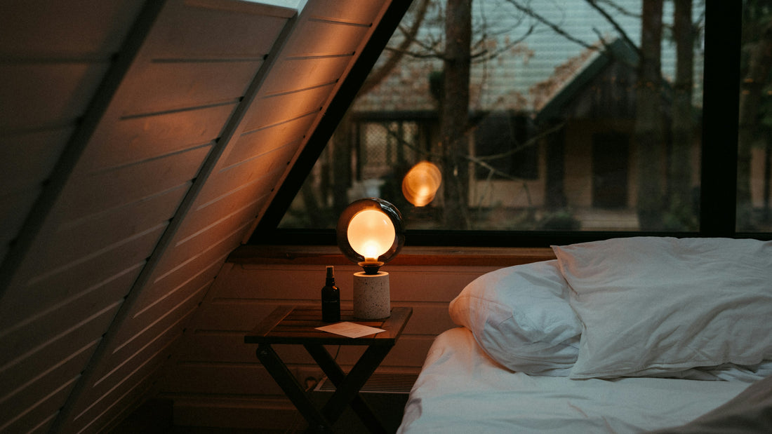 Dim cabin bedroom at dusk with a glowing bedside lamp